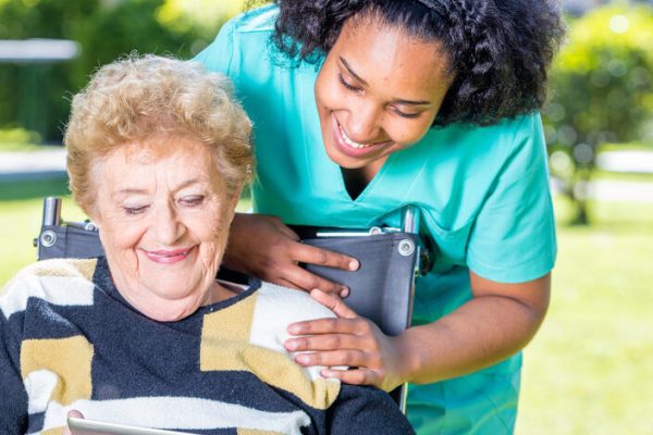 Nurse explaining tablet use to elder woman on wheelchair.